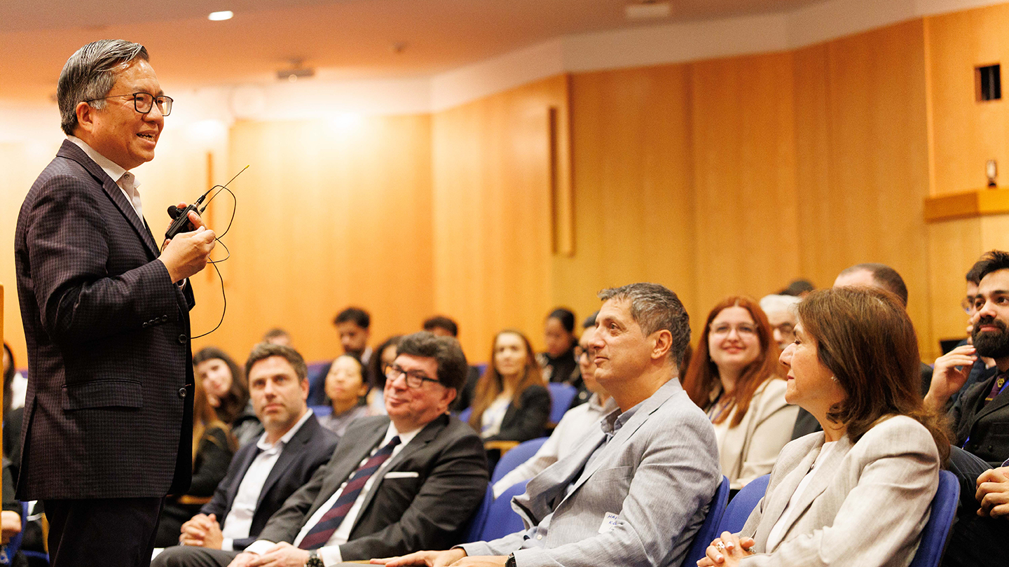 A speaker stands near the front row, talking to an audience seated in an auditorium.