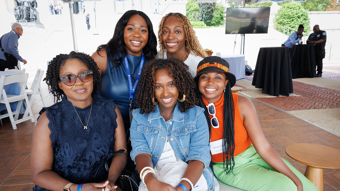 Five alumni smile for a group photo under an event tent, seated and standing close together at a gathering for 2026 Columbia Engineering reunion.