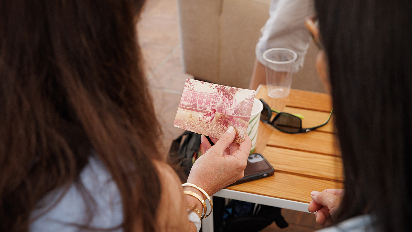 Close-up of an attendee holding a small vintage photo over a café-style table with sunglasses and a phone nearby.