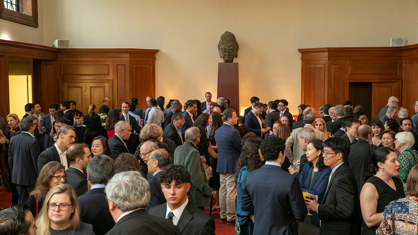 A crowded indoor reception during the Columbia Engineering alumni reunion, with attendees mingling and talking beneath a large sculpture on a pedestal in a wood-paneled room.