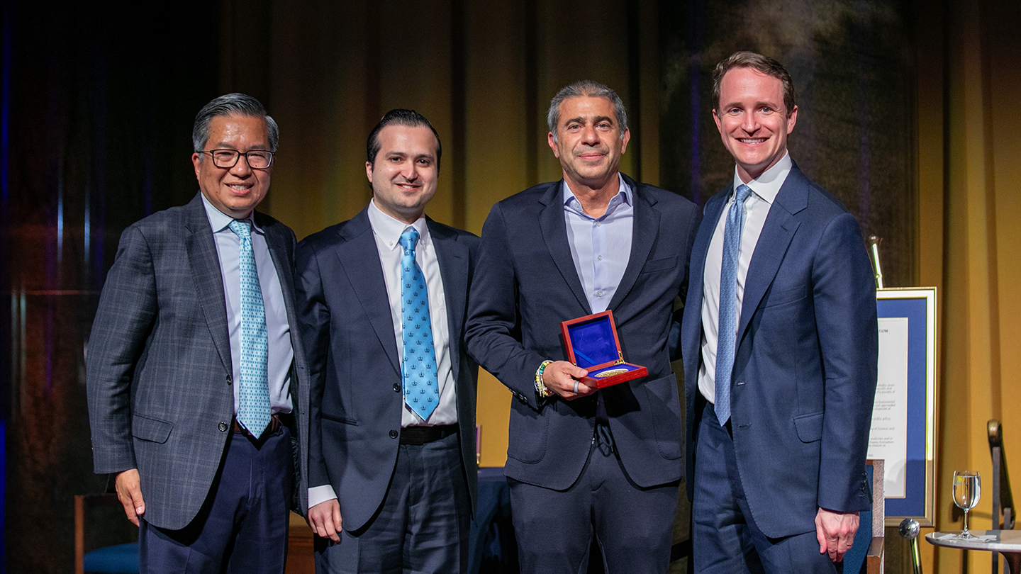 Four men pose onstage at the Columbia Engineering alumni reunion; one holds an open award case with a medal while others stand beside him smiling.
