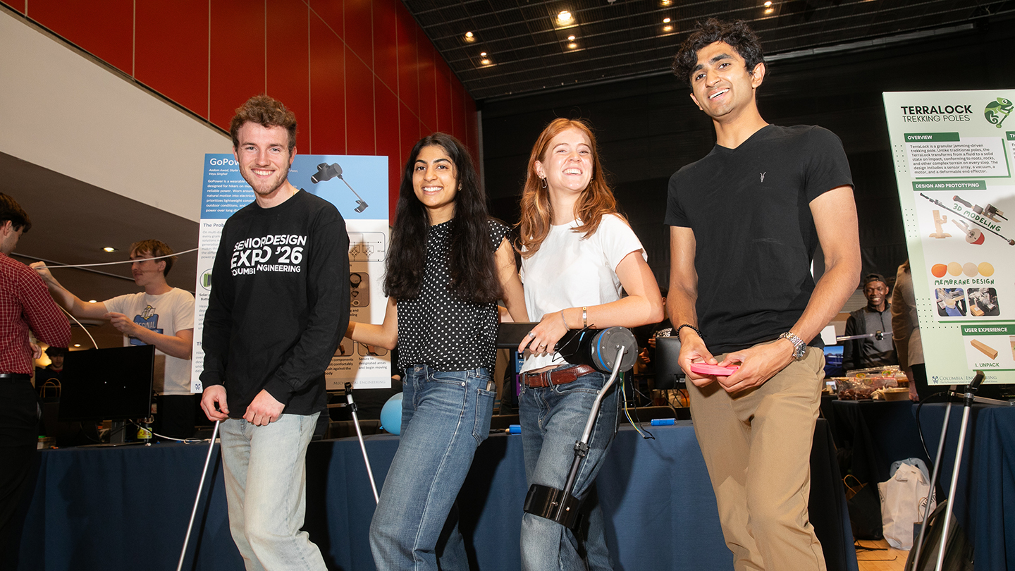 Four students pose in front of project posters at the expo; one holds a wearable device strapped to their leg.
