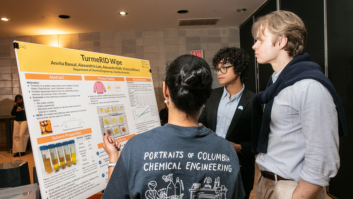 A presenter gestures toward a poster titled “TurmerID Wipe” while two attendees listen at a project display.