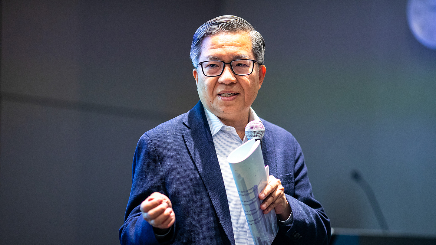 Shih-Fu Chang holds a microphone and rolled notes while addressing the room.