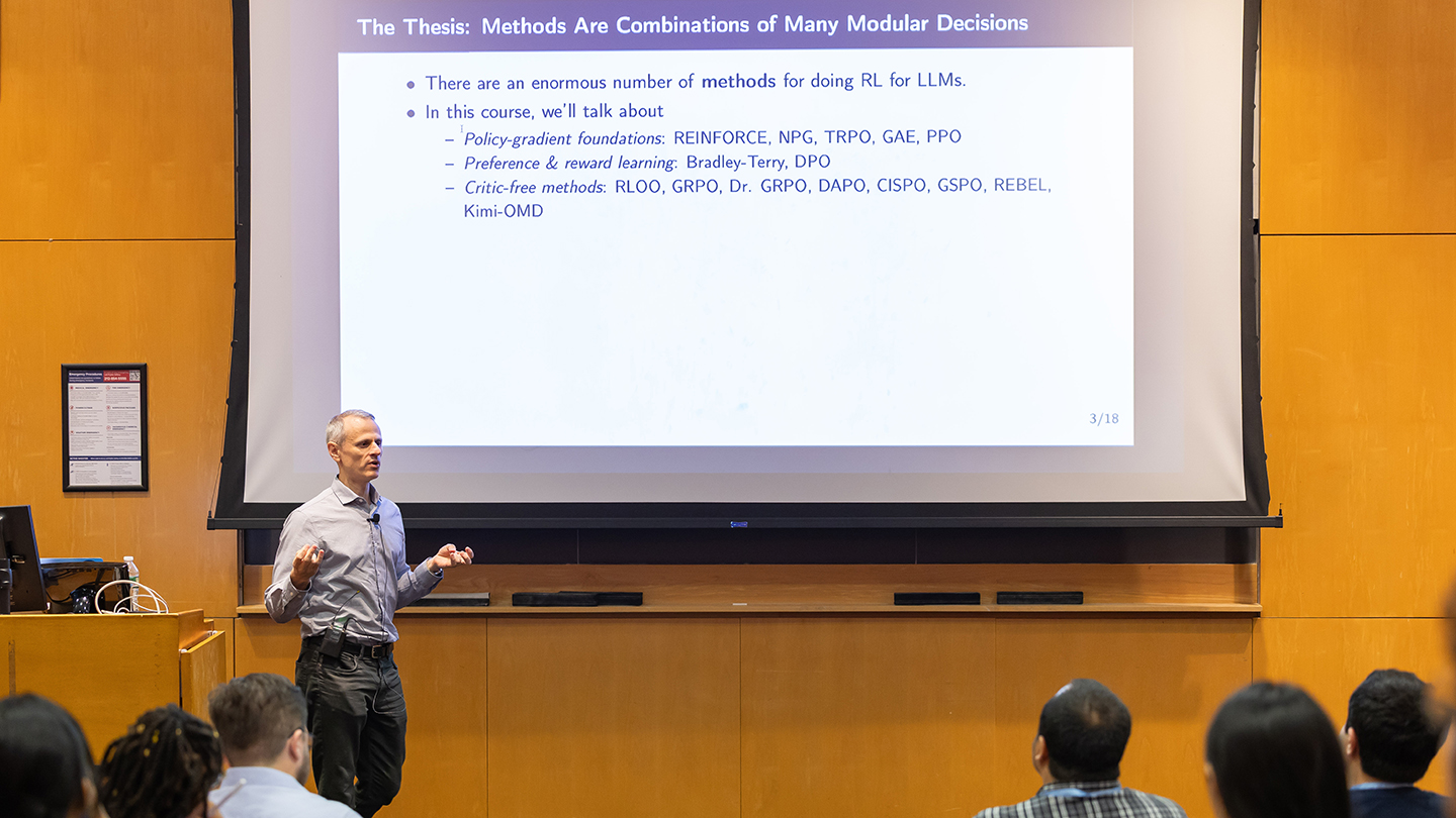 David Rosenberg stands in front of a large screen showing a slide about reinforcement learning methods for LLMs, while attendees watch from the front rows.