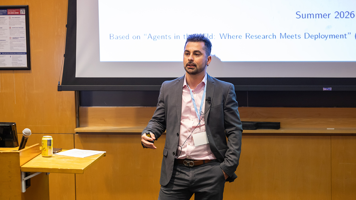 Enrico Santus stands near the front of the room mid-talk, with a projected slide behind him.