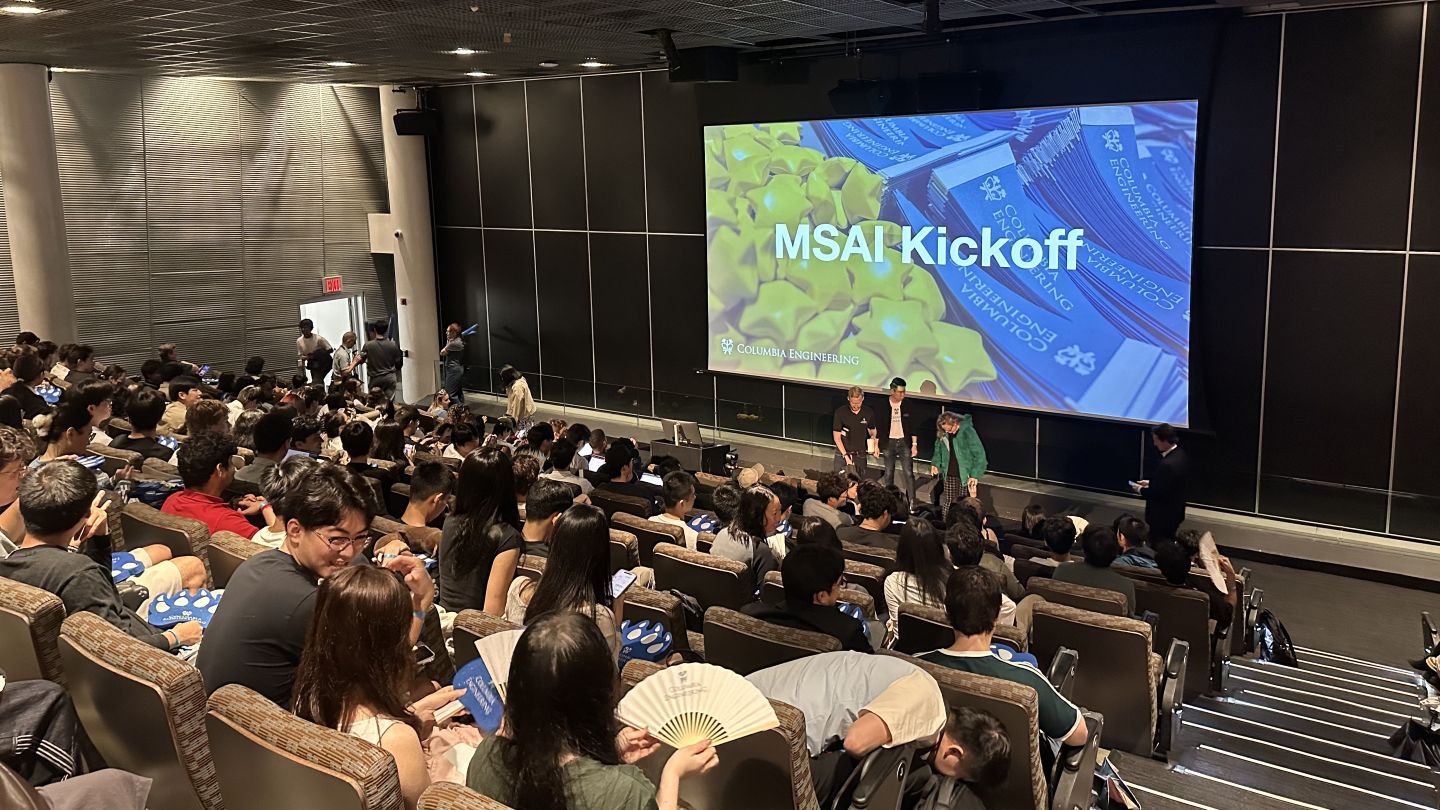 Attendees sit in a lecture hall beneath a large screen displaying "MSAI Kickoff."
