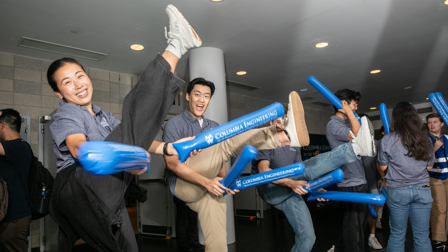 Welcome crew members kick their legs in the air while holding blue Columbia Engineering inflatable sticks.