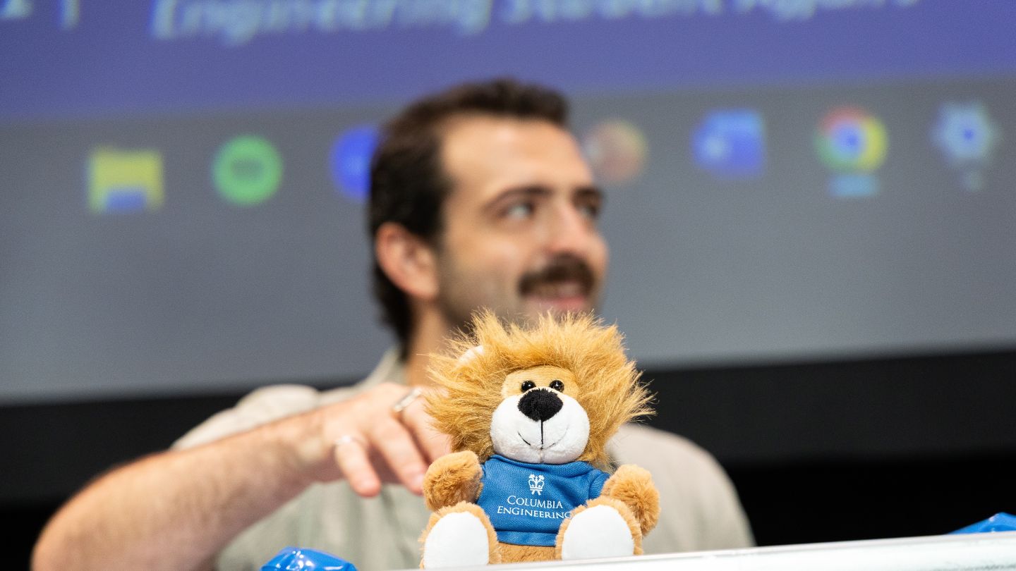 A Columbia Engineering stuffed lion sits in the foreground with an attendee out of focus behind it.