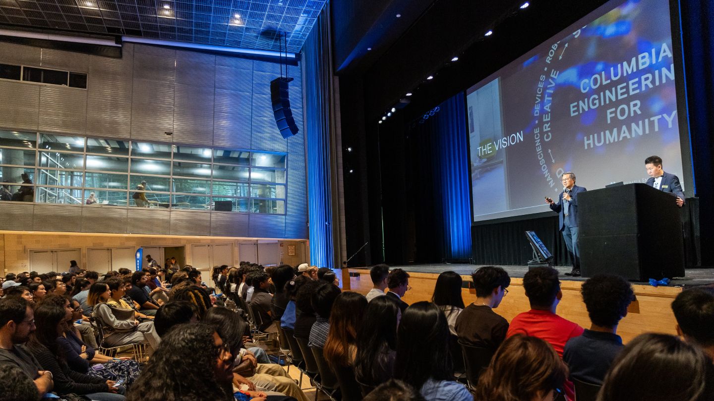 Dean Shih-Fu Chang speaks onstage beside a podium as attendees watch from rows of seats.