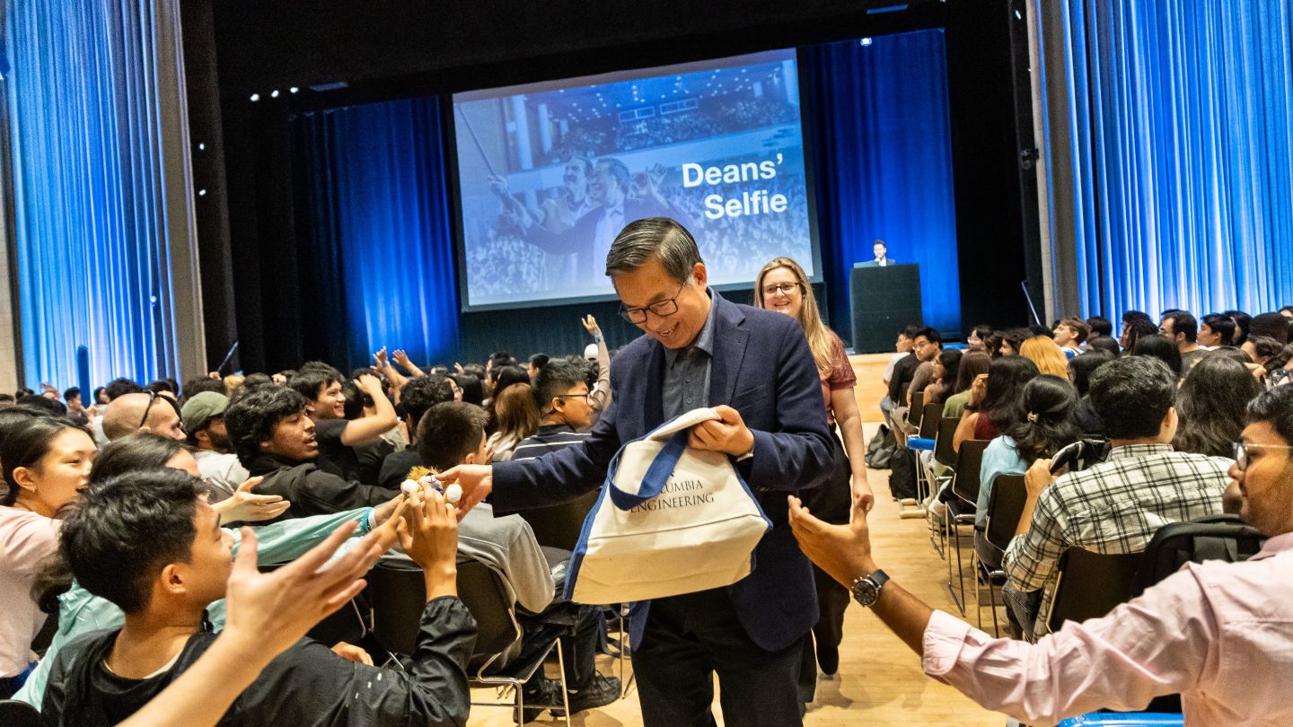 Dean Shih-Fu Chang walks between rows of seated attendees while holding a Columbia Engineering bag.