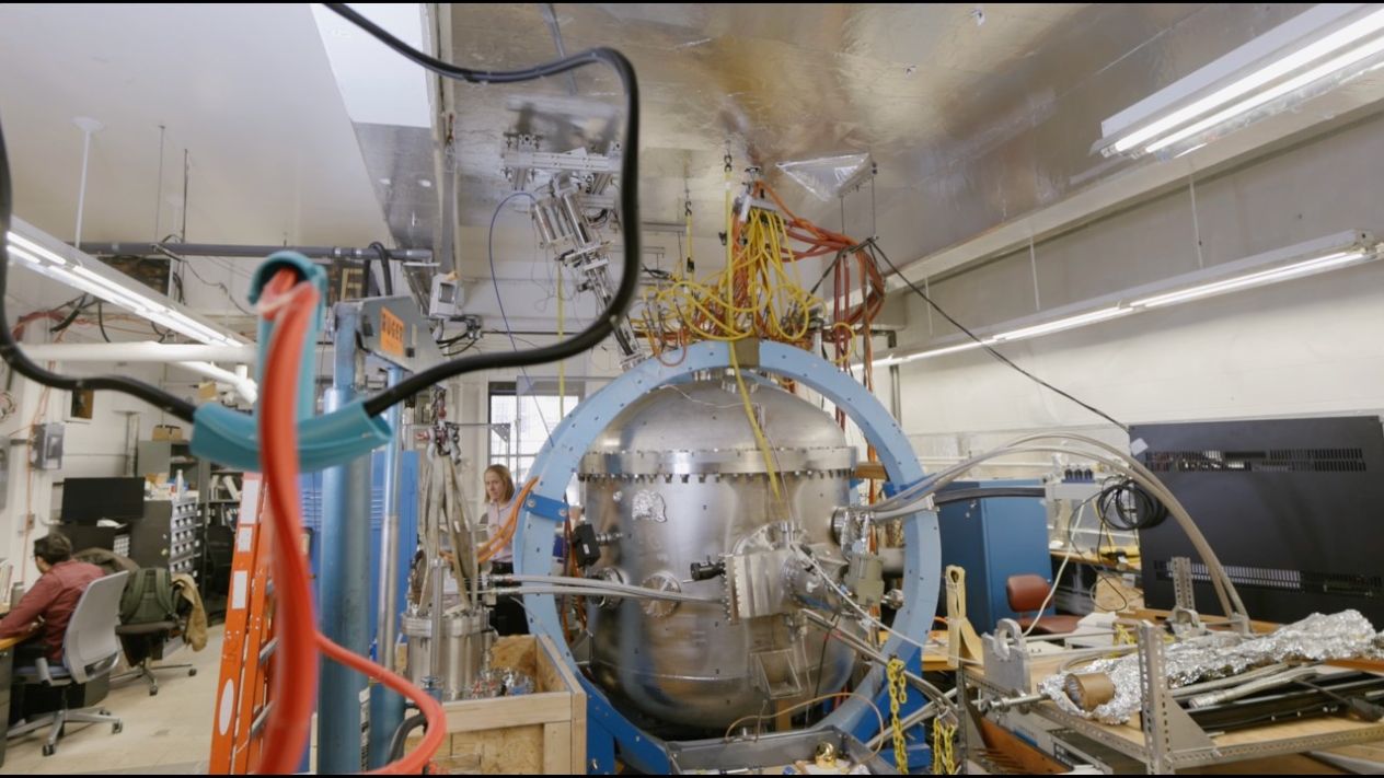 Large metal experimental apparatus surrounded by cables and equipment in a laboratory.