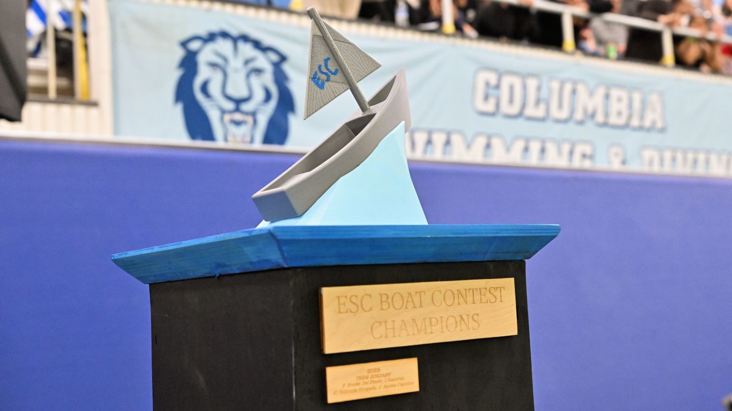 Cardboard boat trophy with a sailboat on top and a plaque reading “ESC Boat Contest Champions.”
