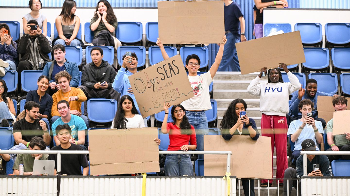 Columbia students hold handmade signs and cheer from the stands during the cardboard boat race.