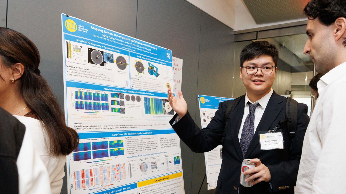 Attendee gestures toward a research poster while discussing it with another attendee during a poster session.