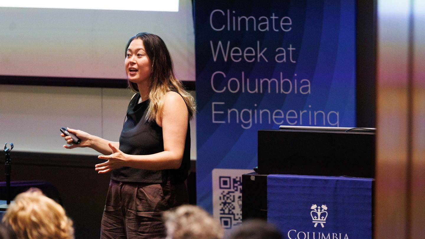 Presenter speaking and gesturing to an audience beside a Climate Week at Columbia Engineering banner.