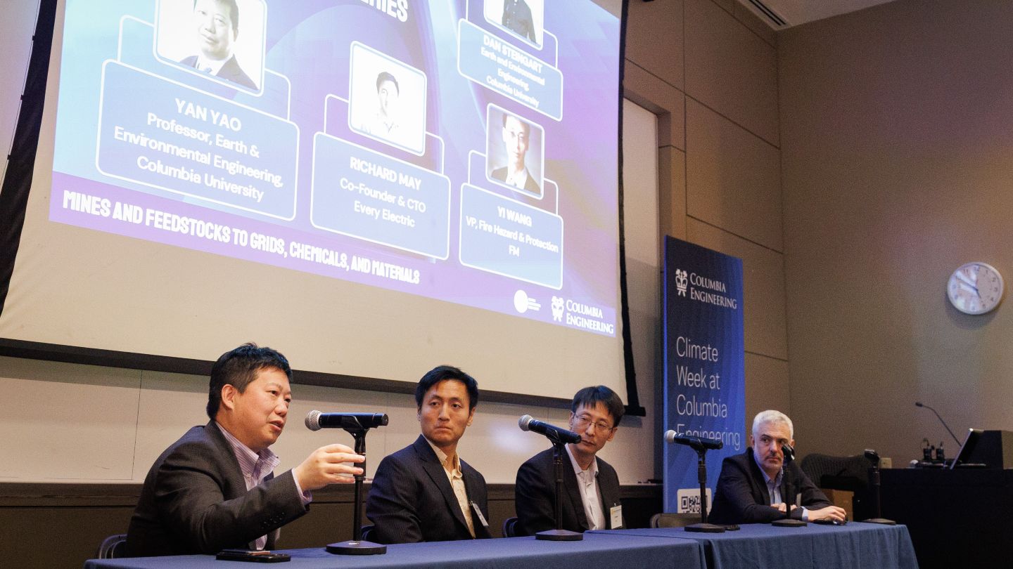 Yan Yao speaking and gesturing while seated with three other panelists, who look toward him, beneath a projected presentation at Columbia Engineering.