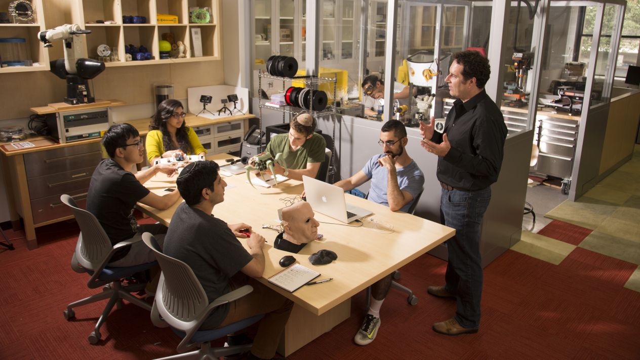 Hod Lipson speaks to students seated around a table working with robotics equipment in a Columbia Engineering lab.