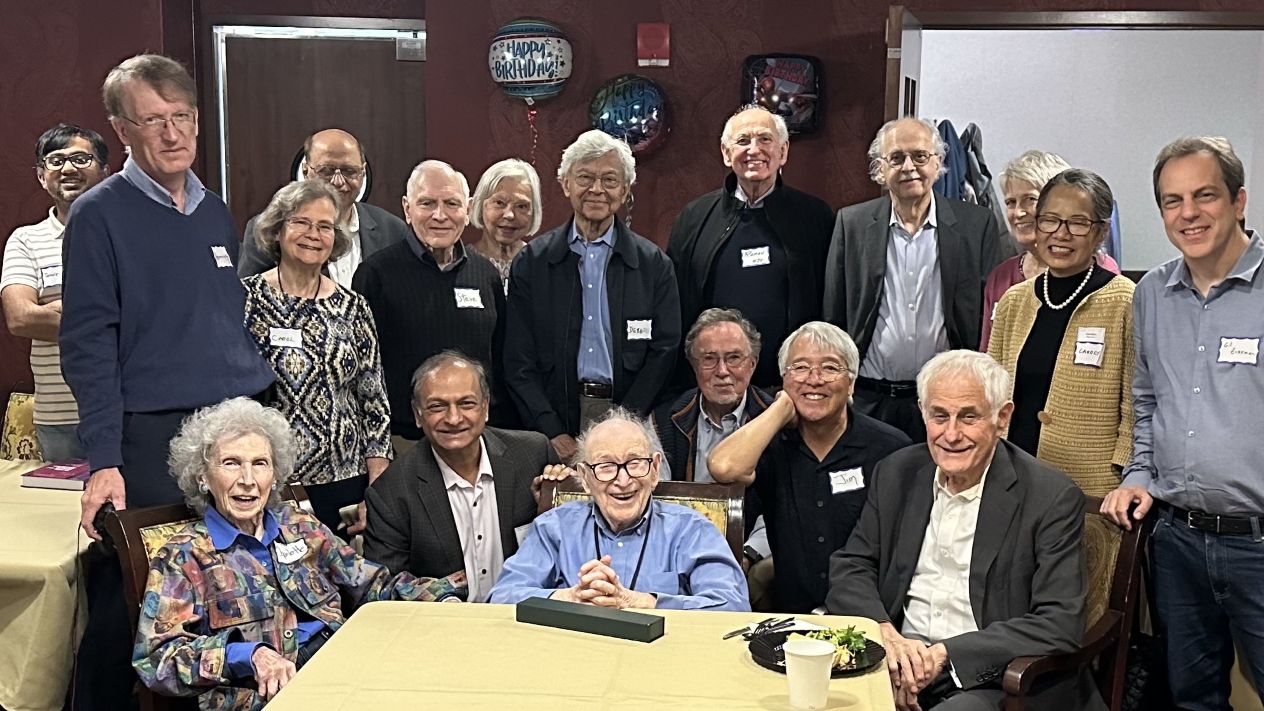 Group of about 18 people posing together at Mischa Schwarz's birthday celebration in a restaurant.