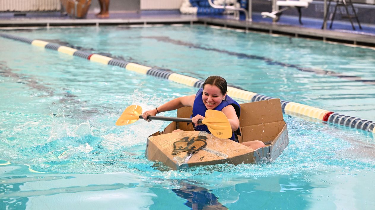 Columbia Engineering student smiles as they paddle a cardboard boat during a race at Uris Pool.