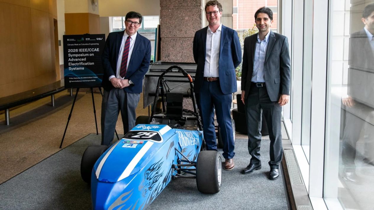 George Deodatis, Matthias Preindl, and Navid Rahbariasr stand beside a blue Columbia University model race car and an IEEE/CCAE Symposium poster.