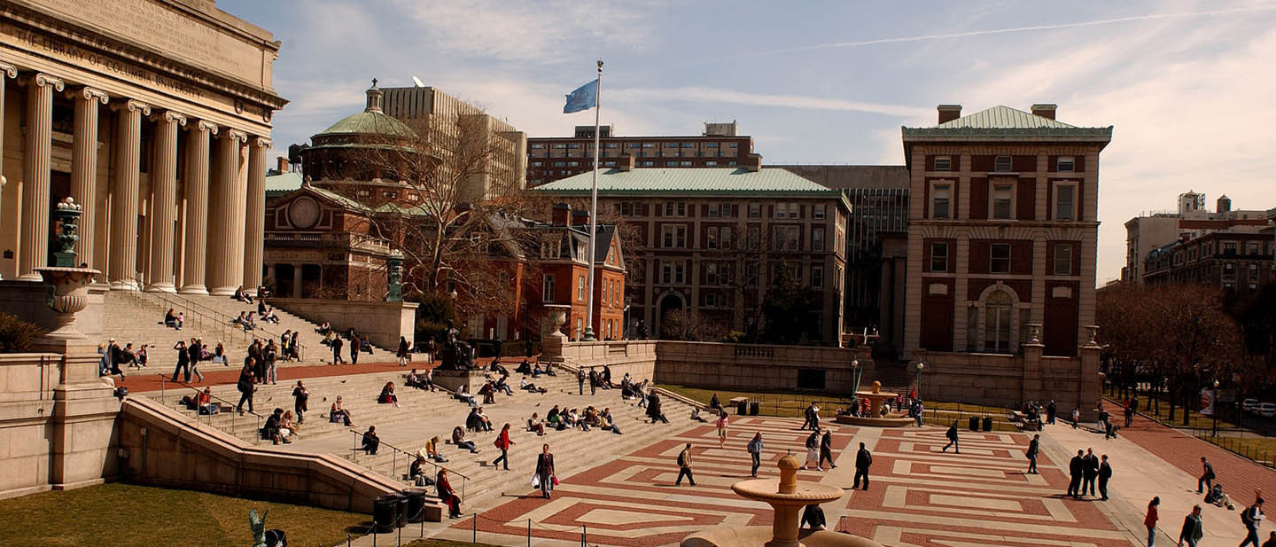 A wide shot of Columbia University campus with students bustling around in a plaza.