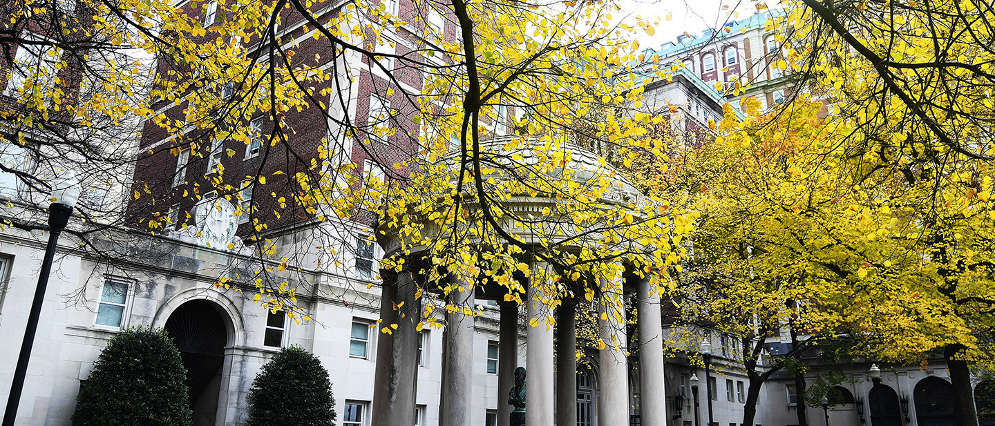 A view of a residence hall on Columbia University's campus with leaves in the foreground.