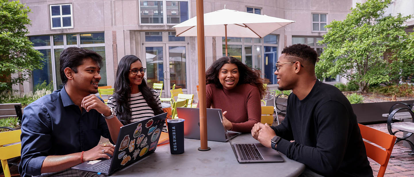Four students sit at a table outdoors on Columbia University's campus.
