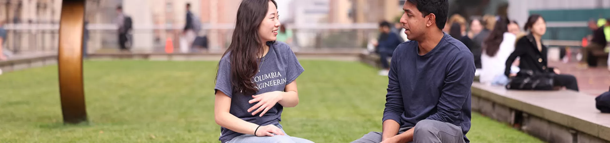 Two Columbia Engineering students sit and talk outdoors.