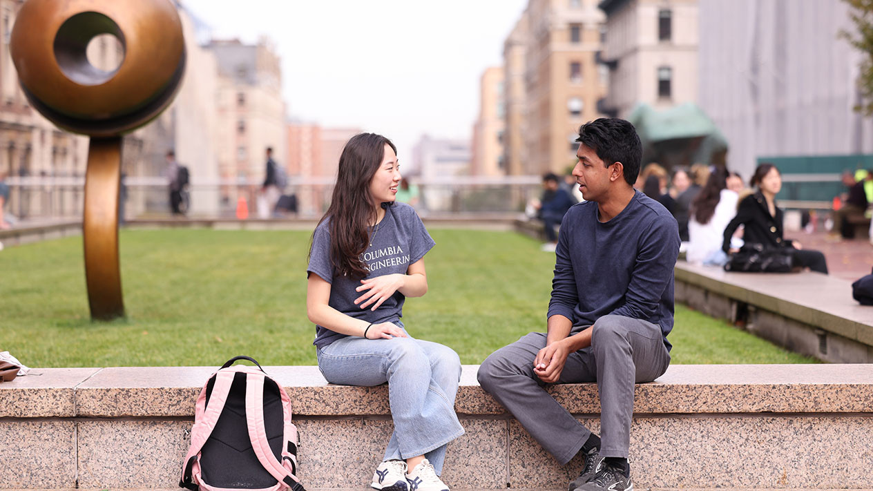 Two Columbia Engineering students sit and talk outdoors.