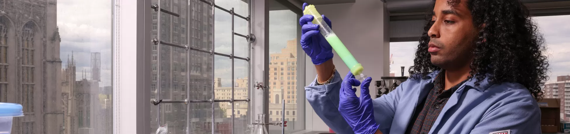 A Columbia Engineering student in a lab coat inspects a test tube in the Obermeyer Lab