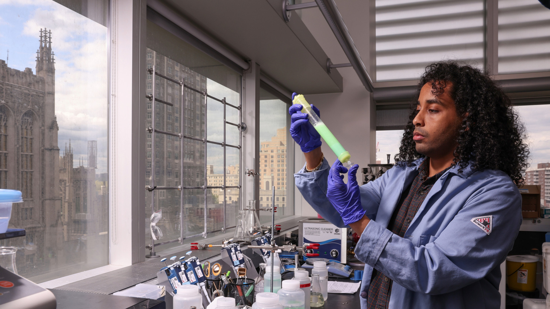 A Columbia Engineering student in a lab coat inspects a test tube in the Obermeyer Lab