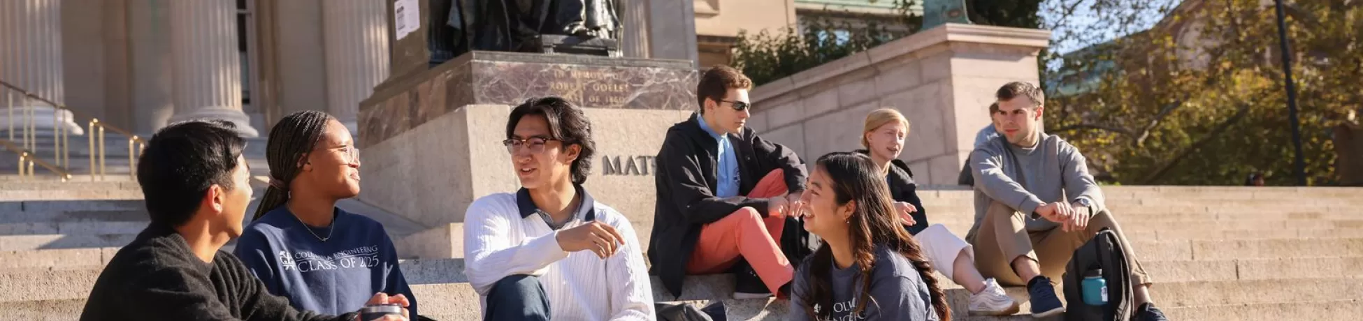 A group of students sit on the steps outside of a Columbia University building.