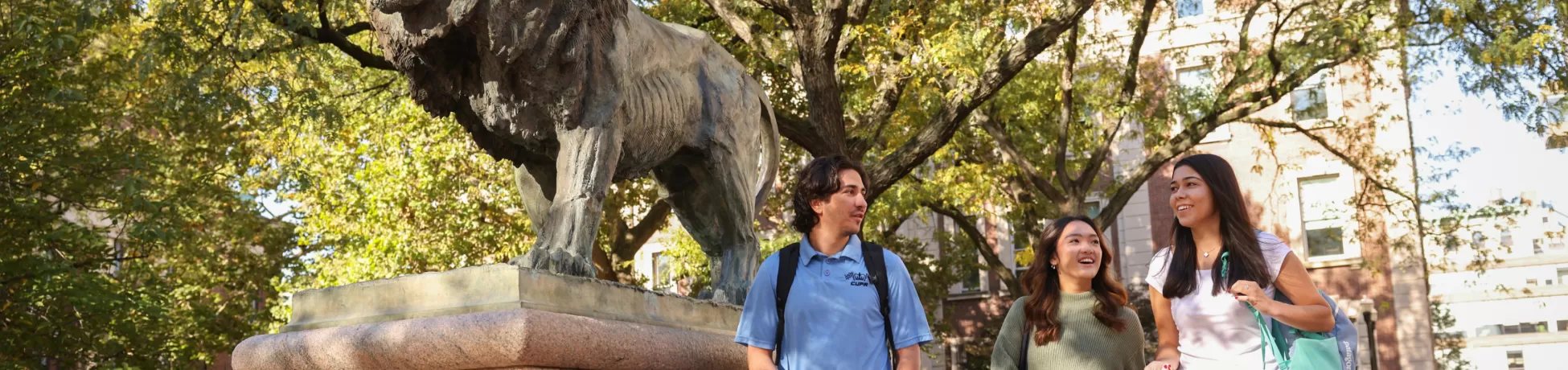 Three Columbia Engineering students talk near the Scholar Lion sculpture.
