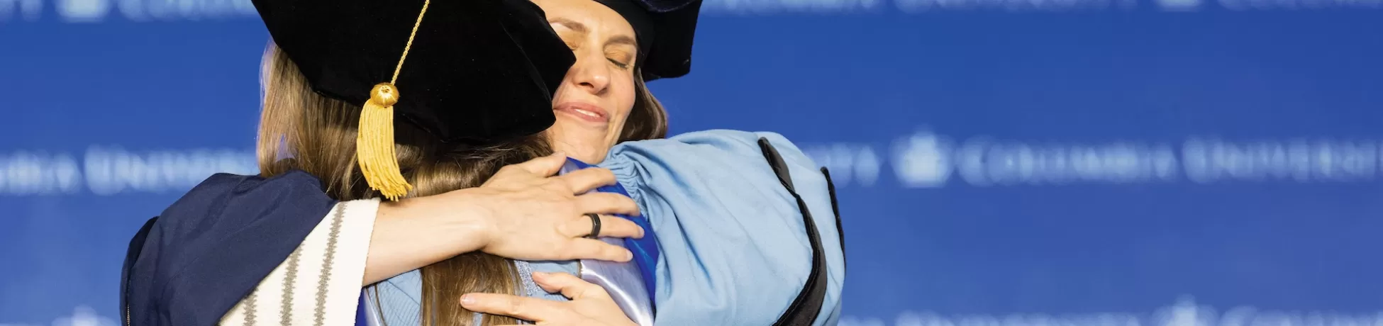 Two people in graduate regalia hugging