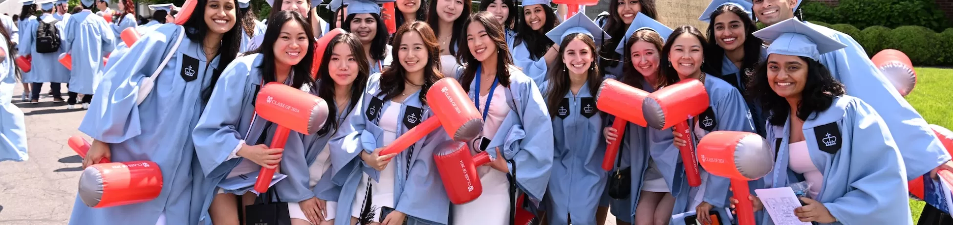 Eighteen Columbia Engineering students in their graduation regalia holding inflatable hammers