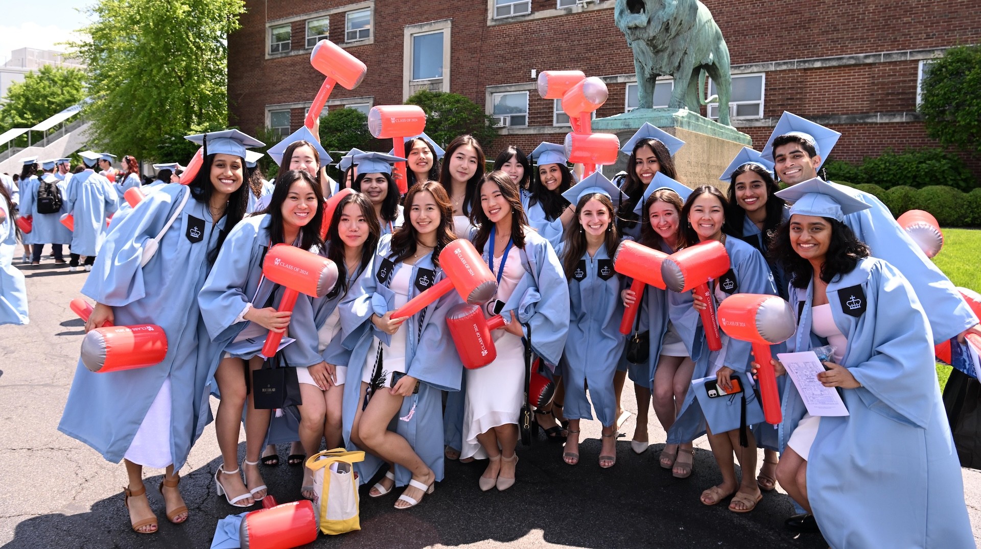 Eighteen Columbia Engineering students in their graduation regalia holding inflatable hammers