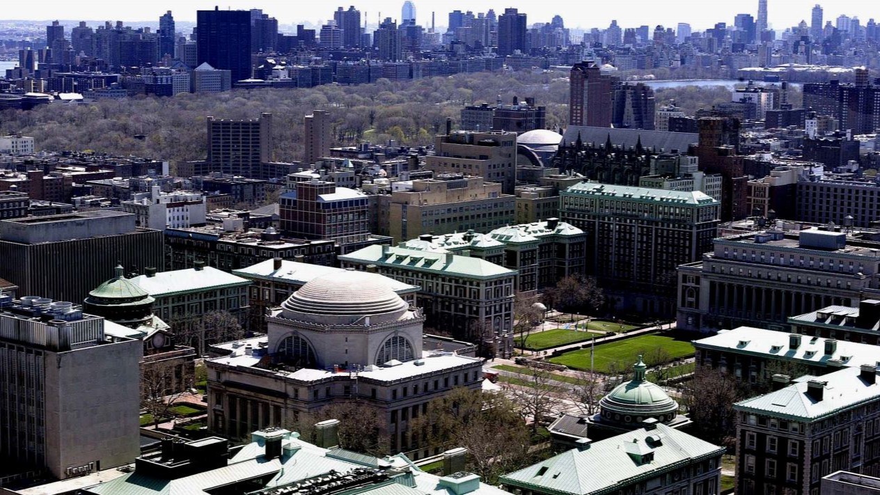 A high-up view of Columbia University and Barnard College in front of downtown Manhattan
