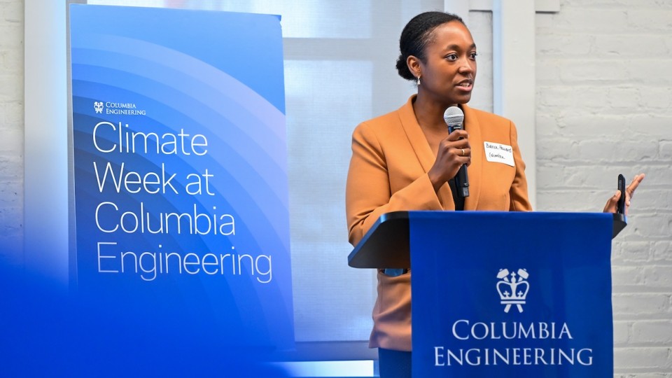 A person speaking into a microphone in front of a podium. The banner behind them reads "Climate Week at Columbia Engineering"