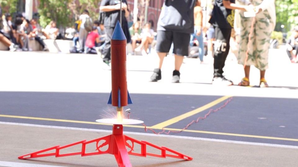 image of a red model rocket lifting off from platform