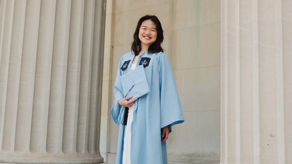 A woman posing for a photo in Columbia University graduation regalia