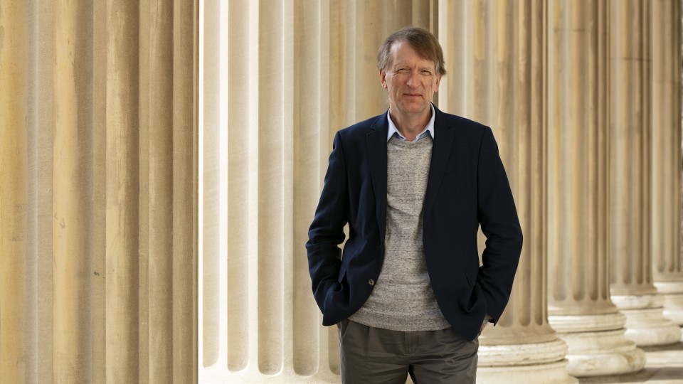 Henning Schulzrinne posing for a photo with his hands in his pockets in front of a row of classical pillars.