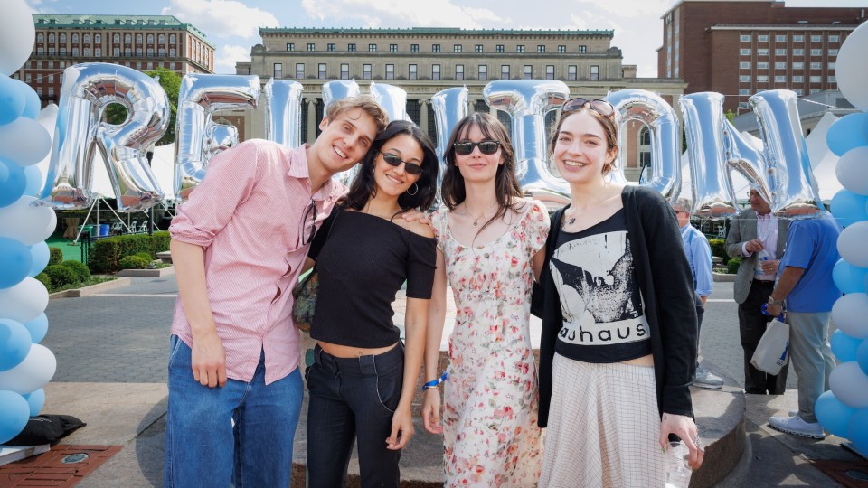  Four people smile for a photo in front of a large balloon during the Columbia Engineering reunion on campus.