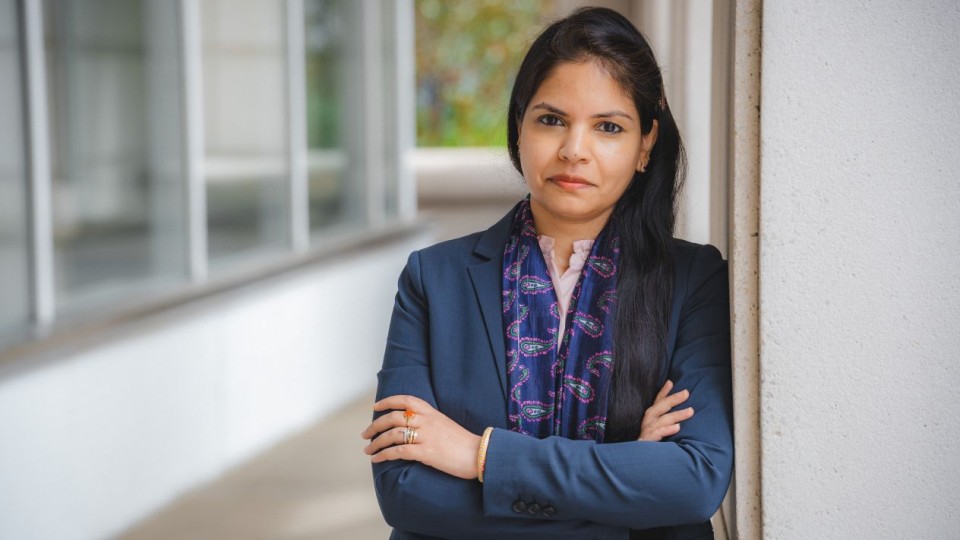 Greeshma Gadikota posing with arms crossed in a dark blue suit in a glass-lined hallway