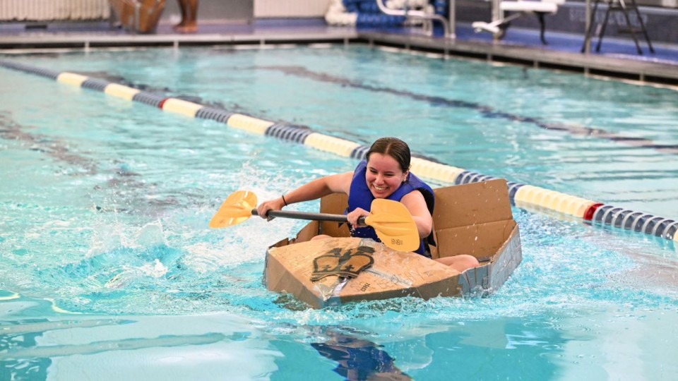 Columbia Engineering student smiles as they paddle a cardboard boat during a race at Uris Pool.