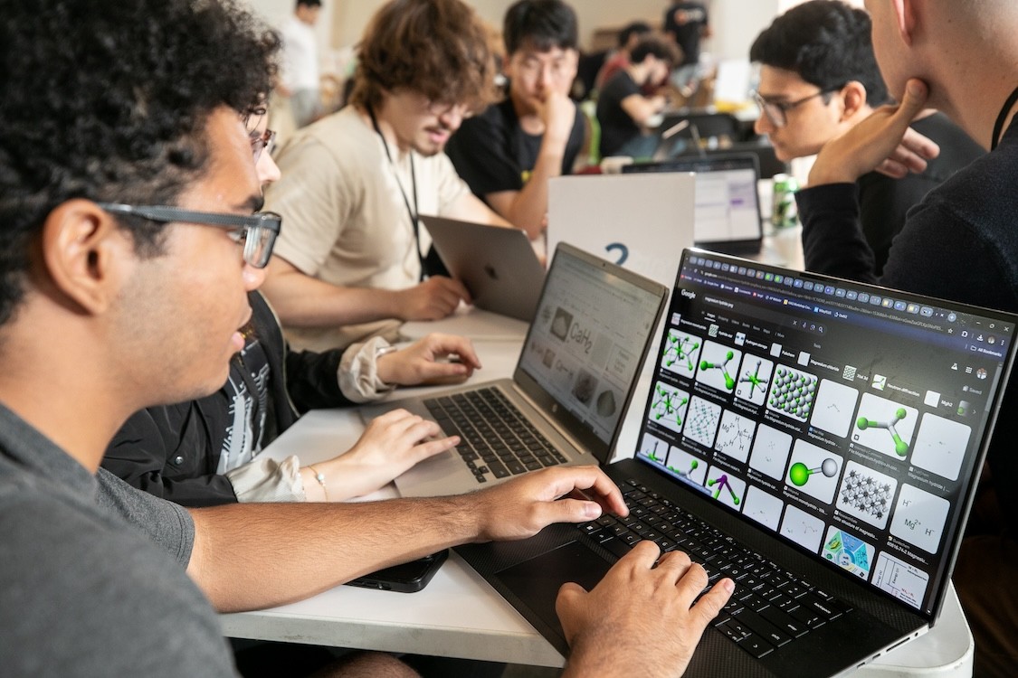 A student types at their laptop. The screen shows images of crystal structures.
