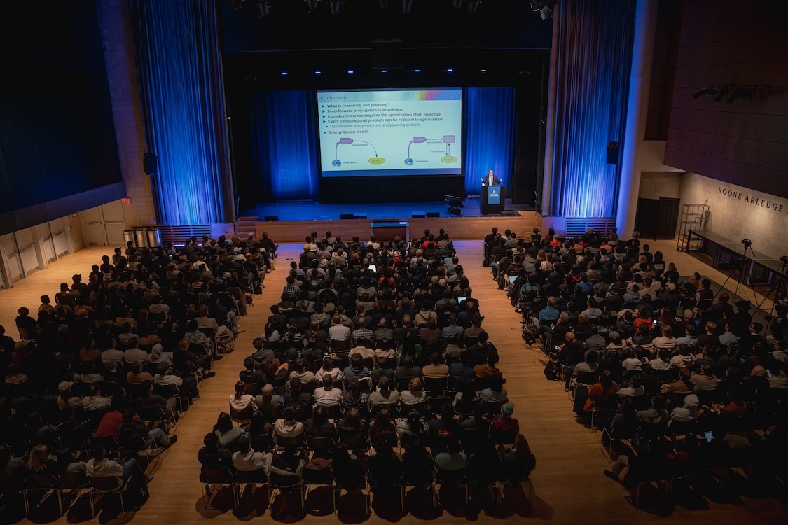 A bird's eye view of a crowd looking towards the stage as Yann Lecun presents
