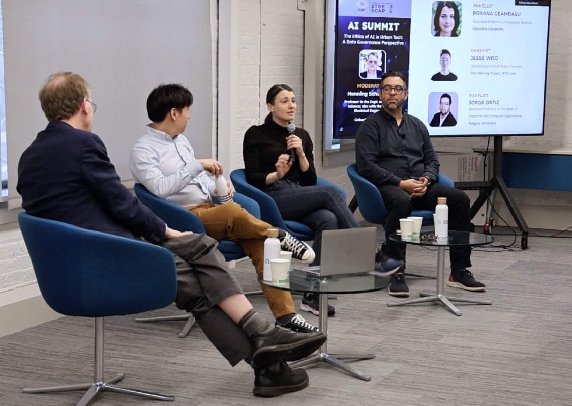 Four presenters sitting in chairs at the front of a room.
