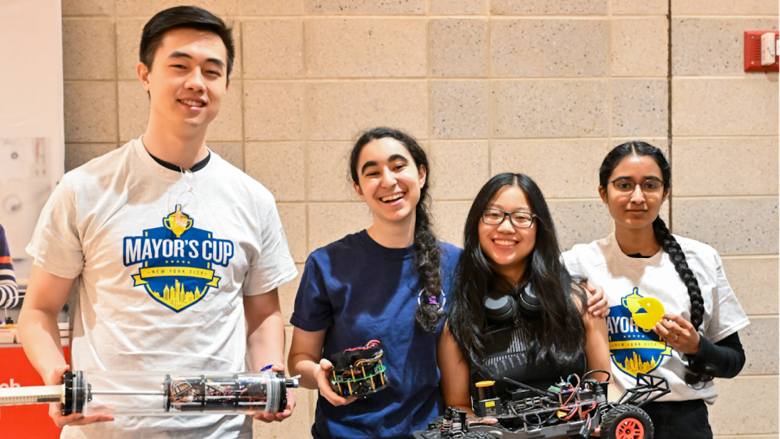 Four high-school students holding robotic components and smiling for a photo