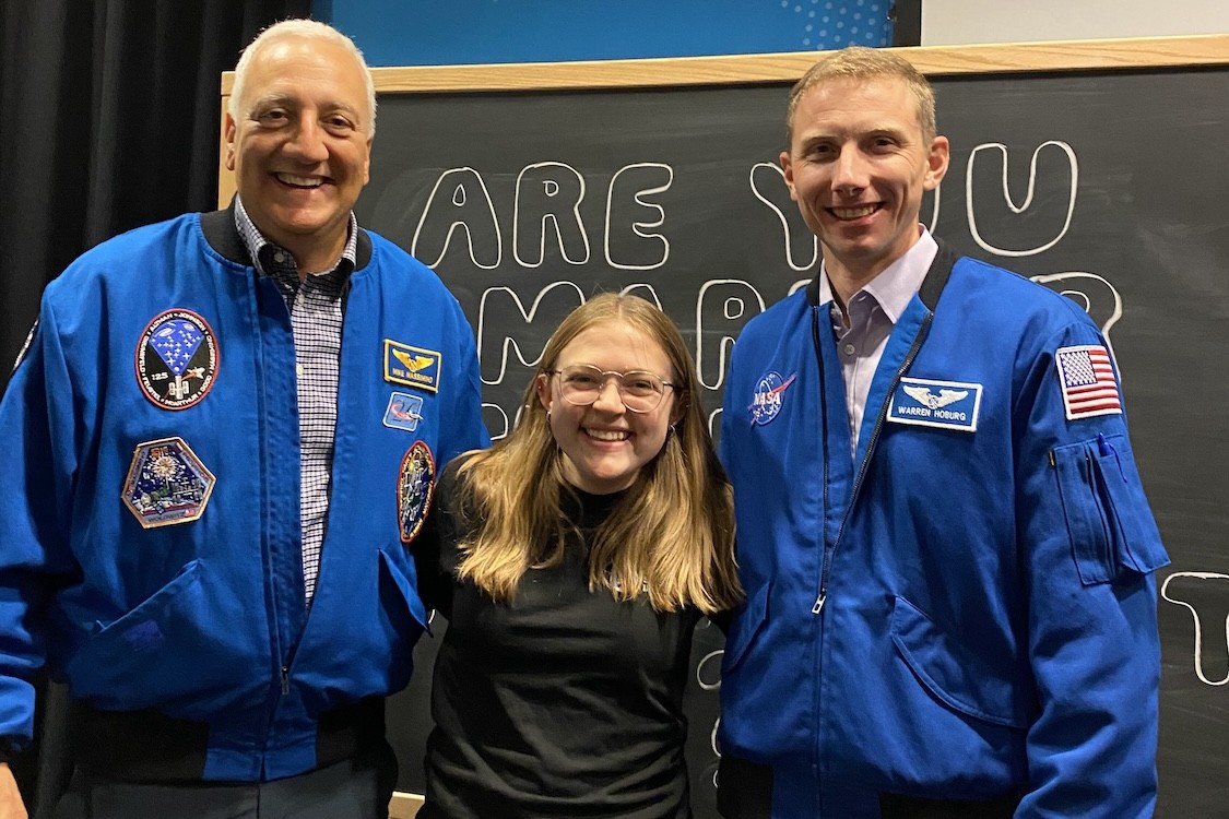 Mike Massimino and Warren Hoburg wear NASA jackets and flank Kate Lampo as they all smile for a photo